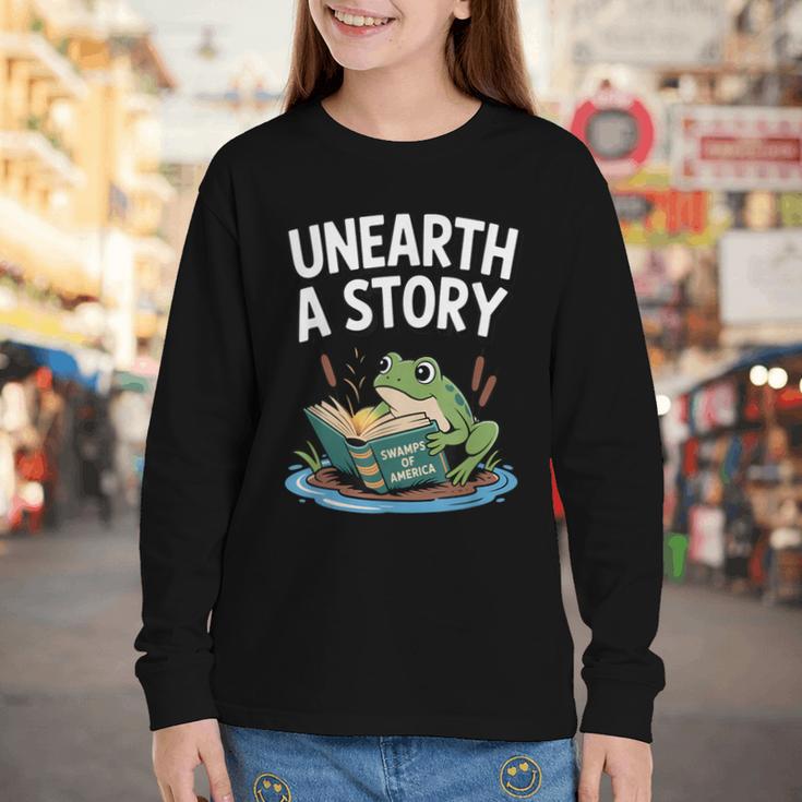 Unearth a Story Frog Reading a Book Summer 2026 Youth Long Sleeve Tee Unearth a Story Frog Reading a Book Summer 2026 Youth Long Sleeve Tee