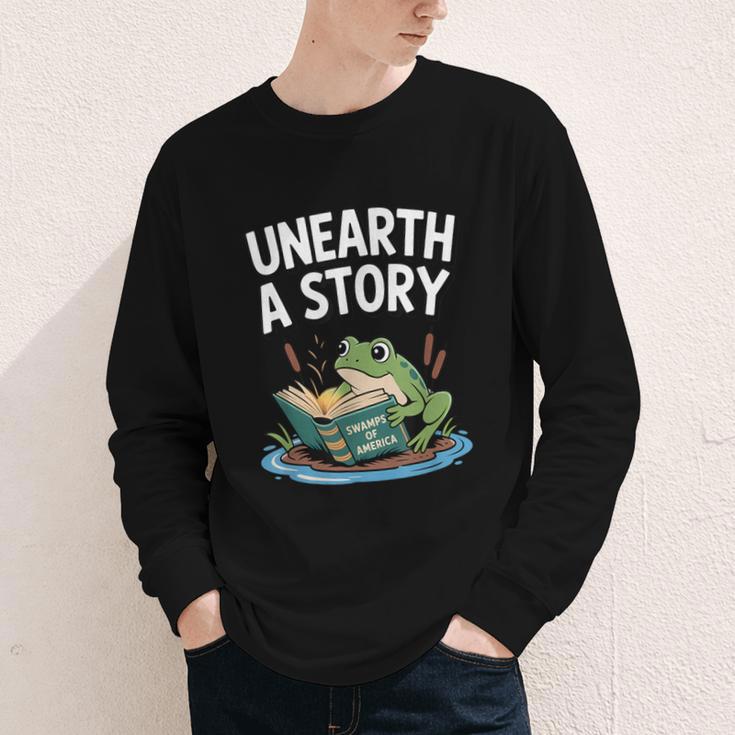 Unearth a Story Frog Reading a Book Summer 2026 Youth Long Sleeve Tee Unearth a Story Frog Reading a Book Summer 2026 Youth Long Sleeve Tee